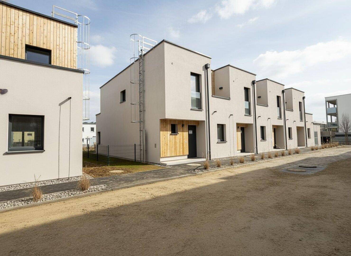 Reihe moderner Reihenhäuser mit heller Fassade, Holzverkleidung und Zugang zum Gartenbereich.