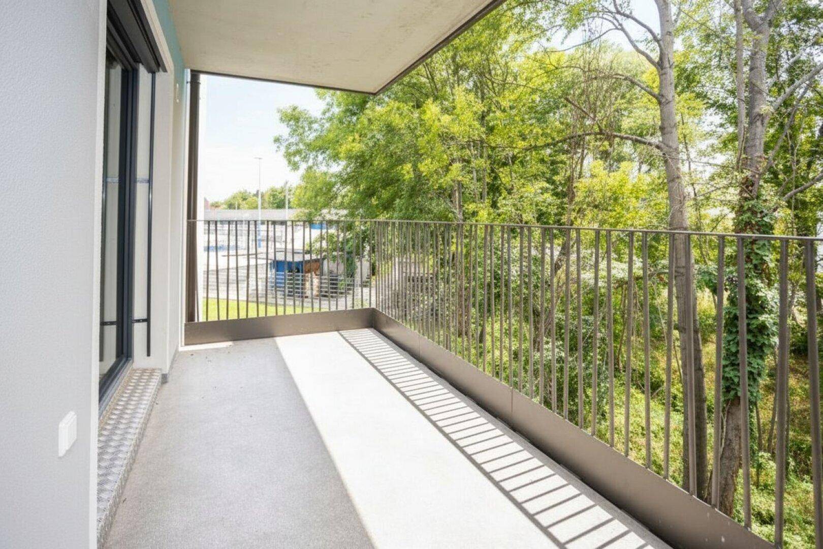 Langer Balkon mit modernem Geländer und Ausblick auf Bäume und Umgebung.