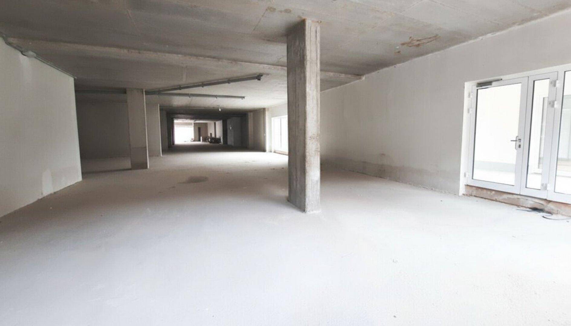 Großer, offener Gewerberaum im Rohbauzustand mit Betonboden und Säulen, bereit für den Ausbau.