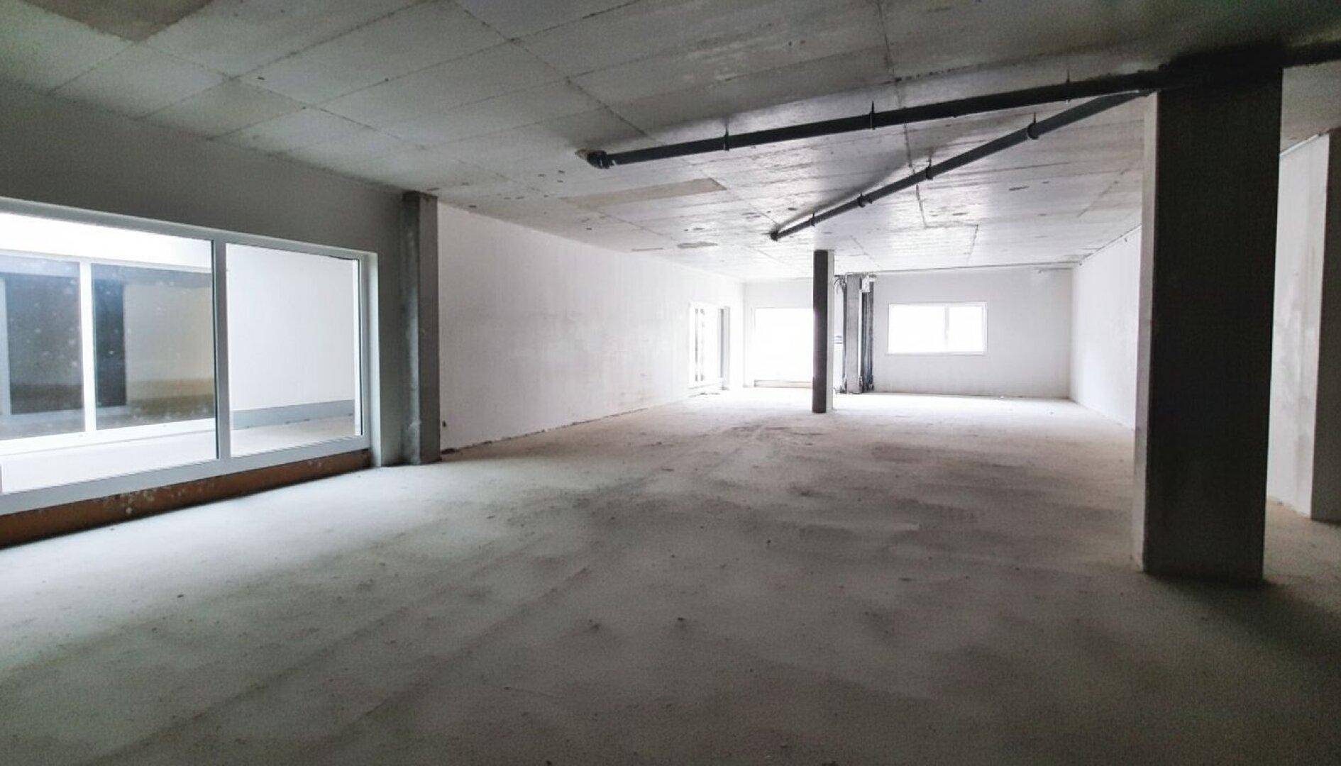 Heller, offener Gewerberaum im Rohbau mit großen Fensterfronten und sichtbaren Installationen an der Decke.