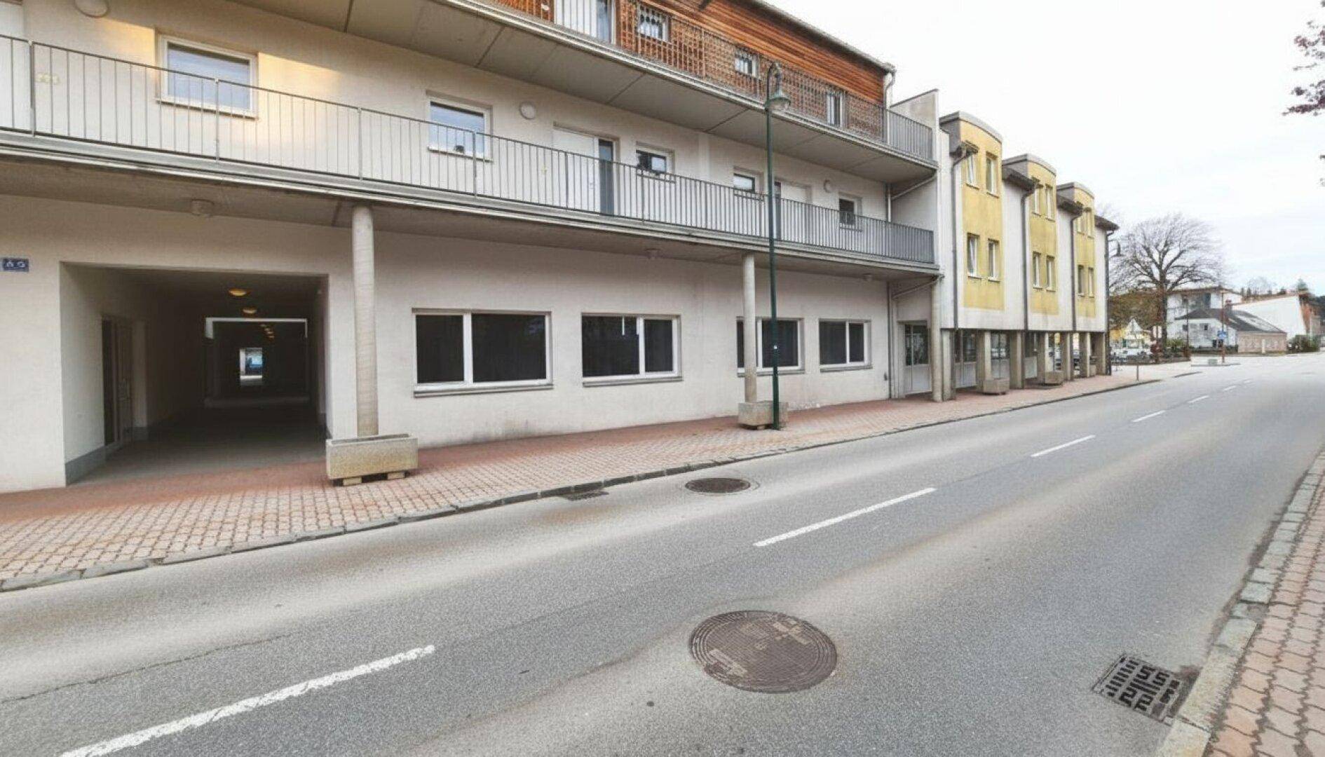 Gebäudekomplex mit Geschäften im Erdgeschoss und Wohnungen darüber, entlang einer Straße.