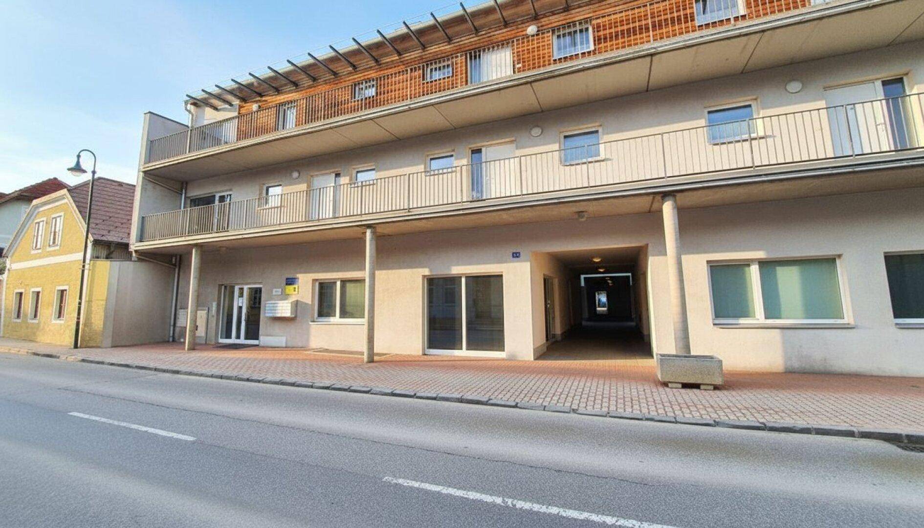 Moderne Gebäudefassade mit Balkonen und Geschäften im Erdgeschoss an einer ruhigen Straße.