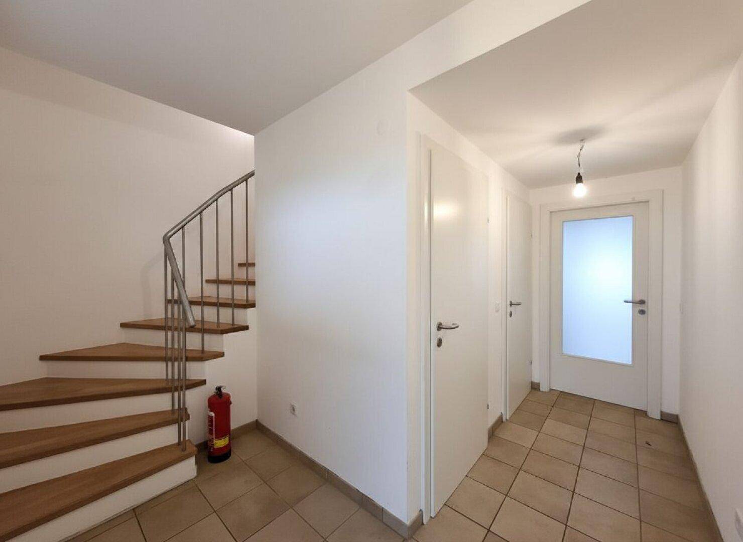 Eingangsbereich mit Holztreppe, Fliesenboden und Zugang zu weiteren Räumen.