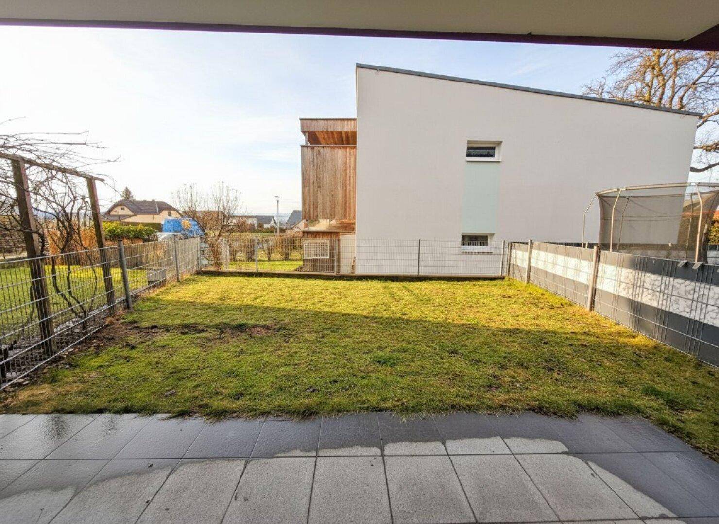 Kleiner Gartenbereich mit Rasenfläche und gepflasterter Terrasse hinter dem Gebäude.