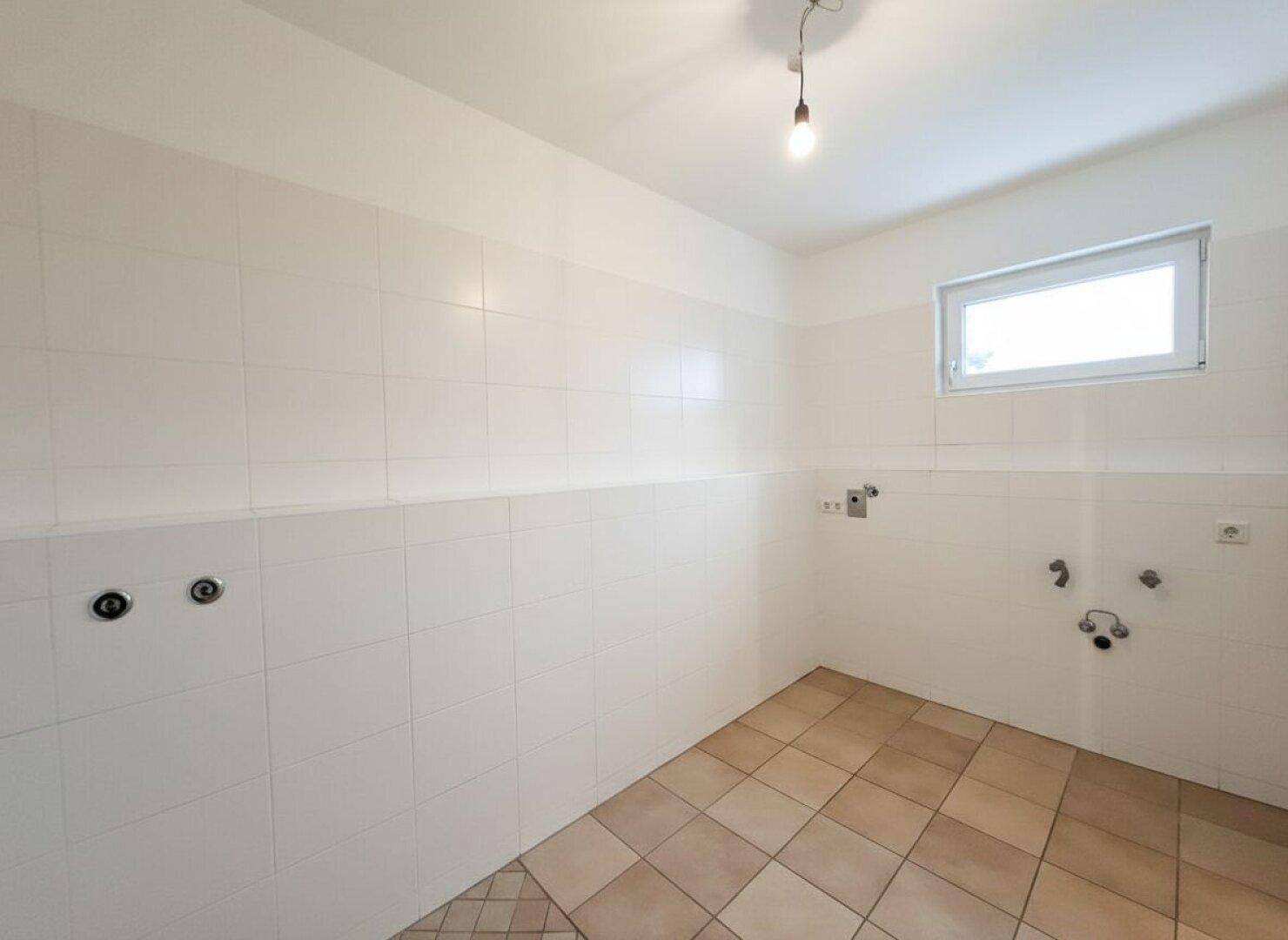 Praktischer Hauswirtschaftsraum mit Fliesenboden, weiß gefliesten Wänden und Fenster.