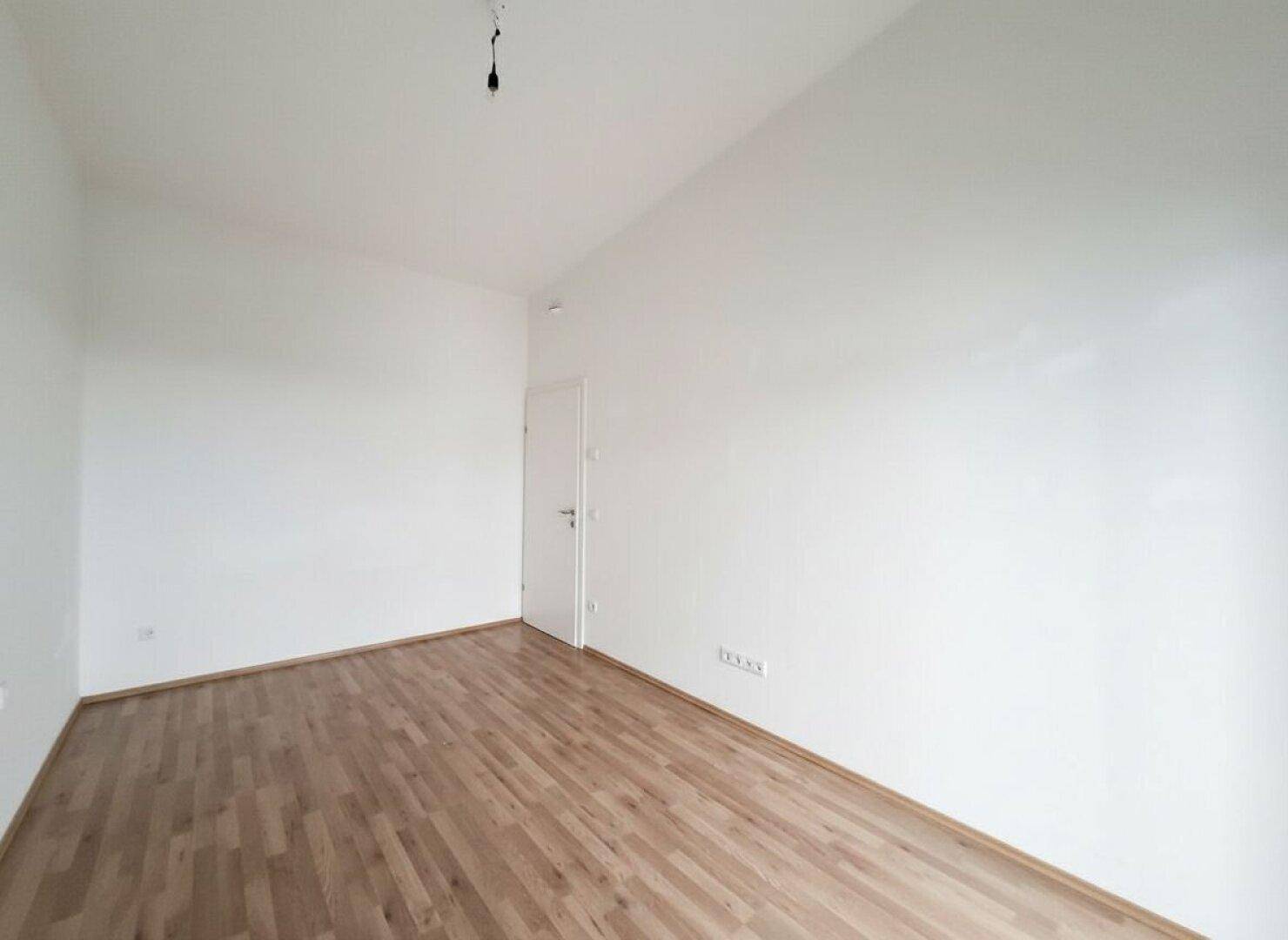 Helles Schlafzimmer mit Parkettboden und schlichten weißen Wänden, ideal für individuelle Gestaltung.