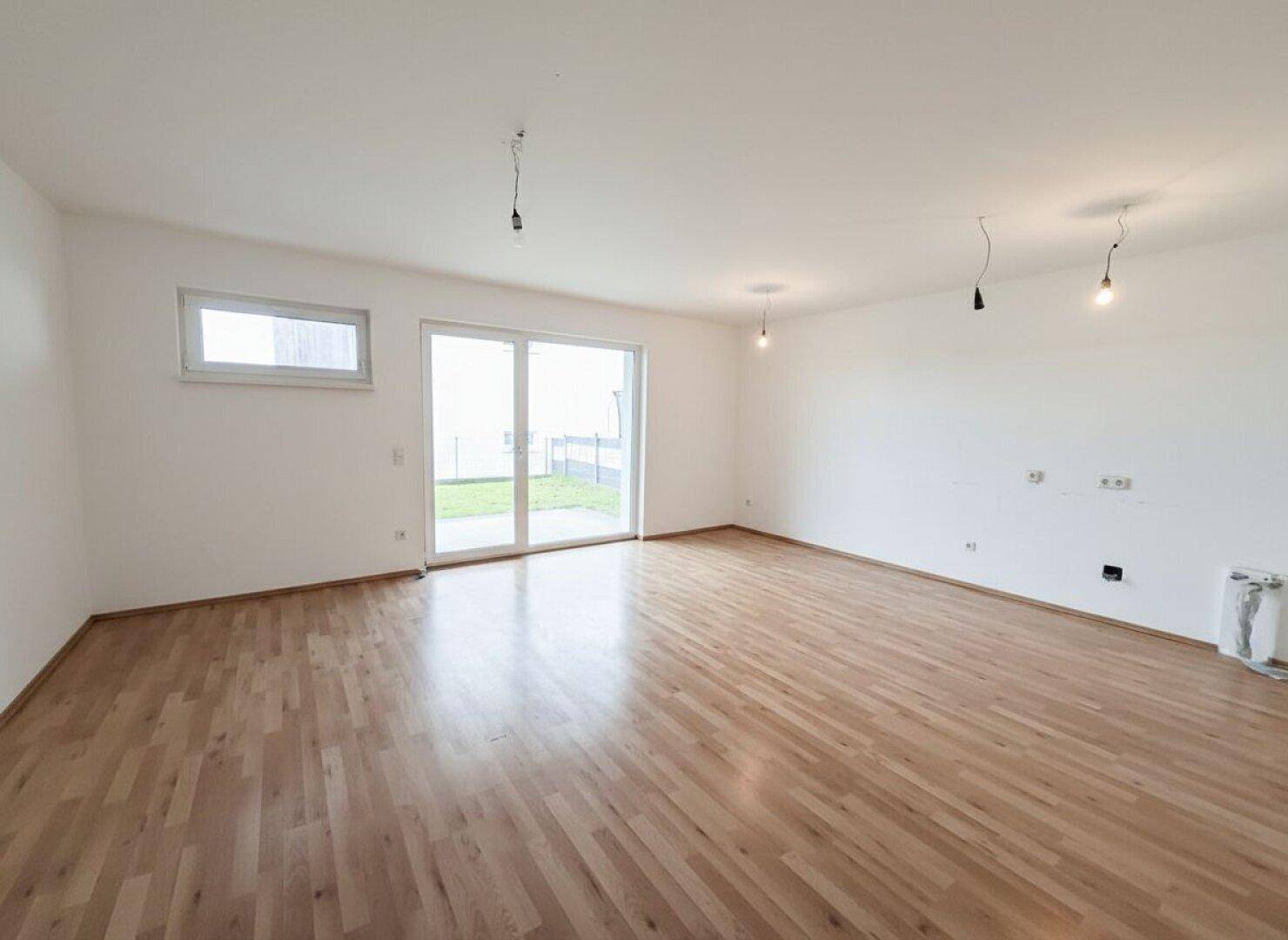 Geräumiges Wohnzimmer mit Holzboden und Schiebetür, die viel Tageslicht hereinlässt.