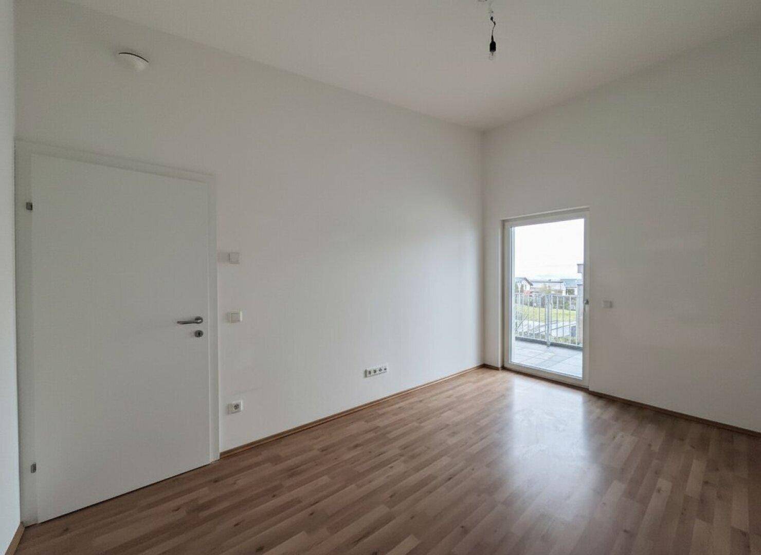 Schlafzimmer mit Parkettboden und Zugang zu einem Balkon, der viel Licht spendet.