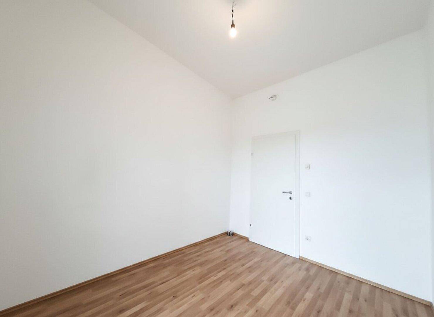 Schlafzimmer mit Parkettboden und schlichten weißen Wänden, bereit für persönliche Einrichtung.