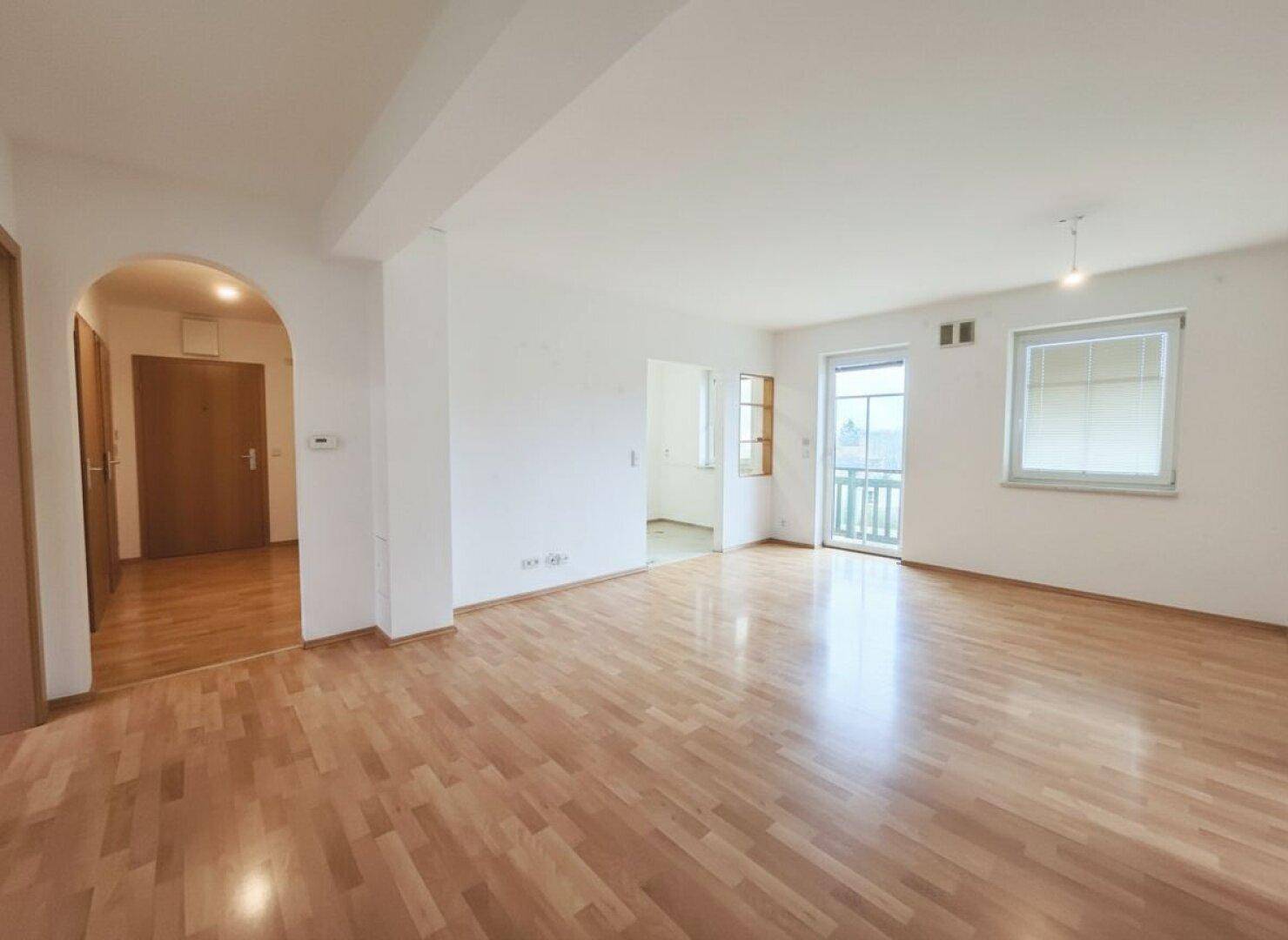 Geräumiges Wohnzimmer mit hellem Parkettboden und Zugang zu einem Balkon, ideal für entspannte Stunden.