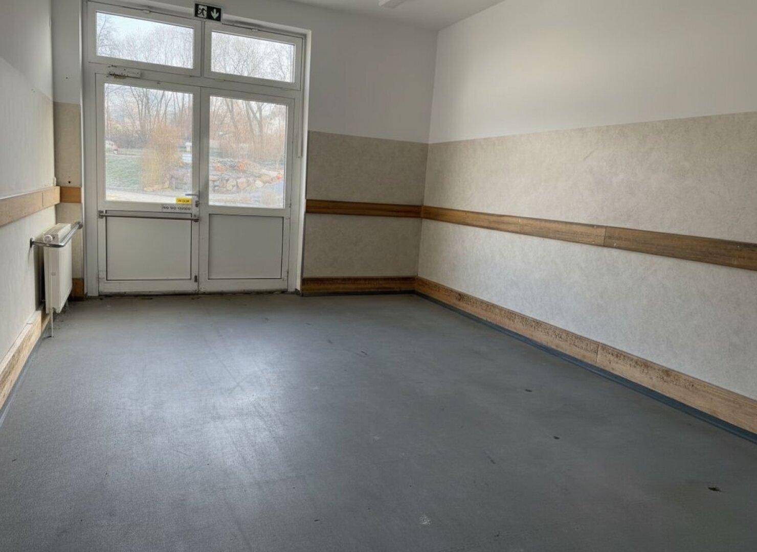 Raum mit großer Glastür, die nach draußen führt, und einer halbhohen Wandverkleidung.