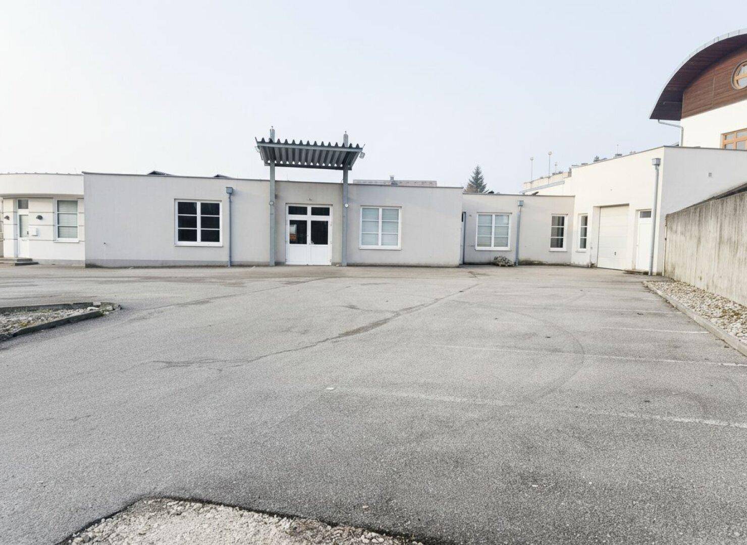 Außenansicht eines Gebäudes mit großem Parkplatz und mehreren Fenstern.