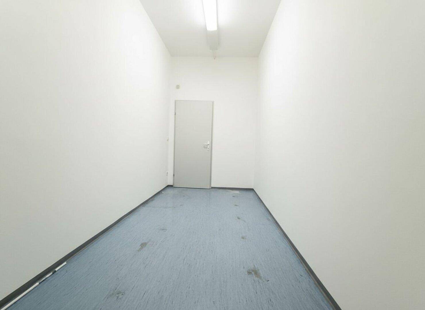 Langer, schmaler Flur mit einer Tür am Ende und einfachem Bodenbelag, gut beleuchtet.