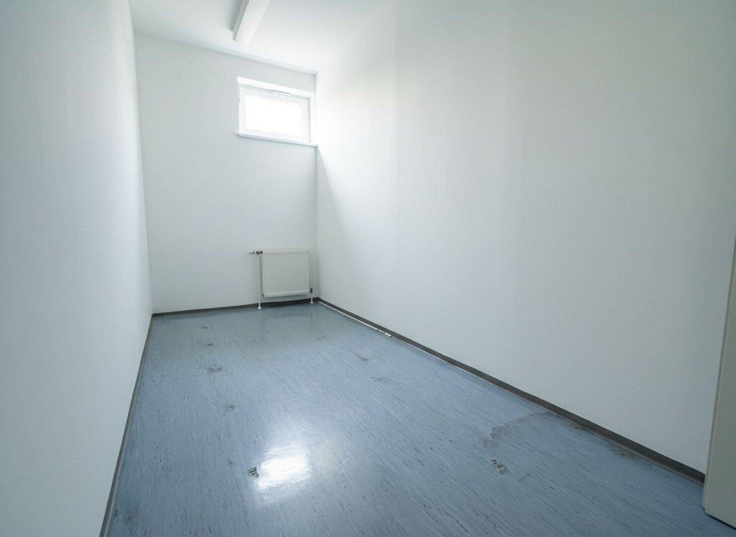 Langer, schmaler Raum mit einem kleinen Fenster und hellem Boden, geeignet als Lager oder Archiv.