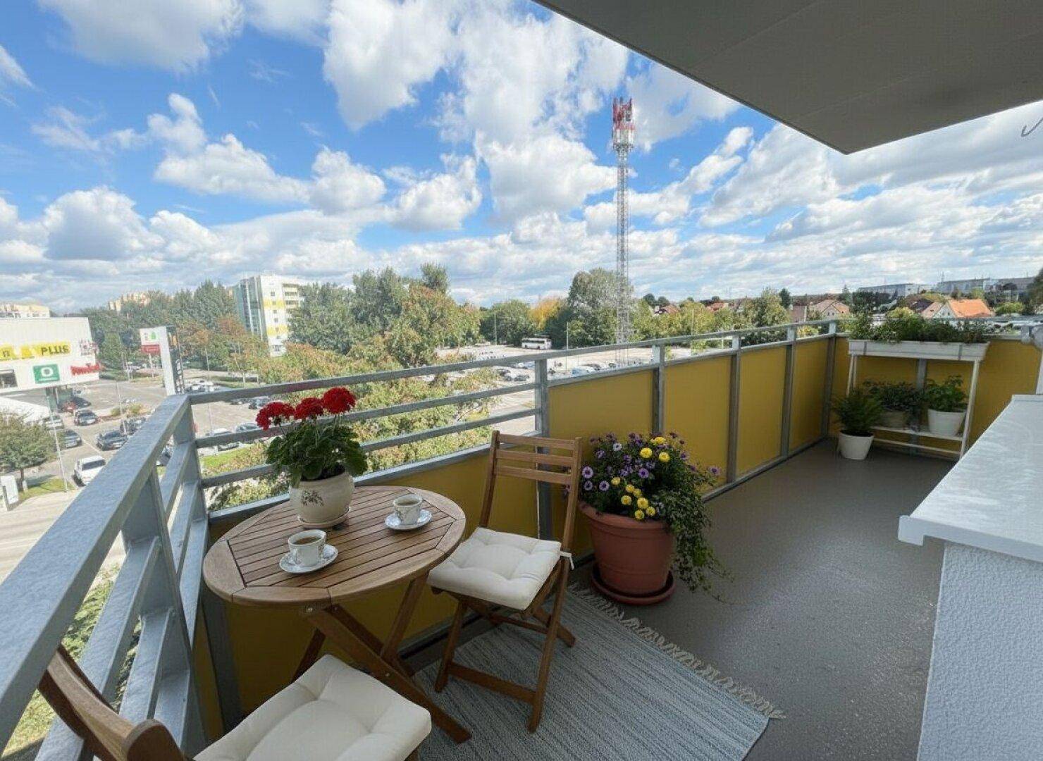 Möblierter Balkon mit gelben Sichtschutzwänden und weitem Blick über die Stadt.