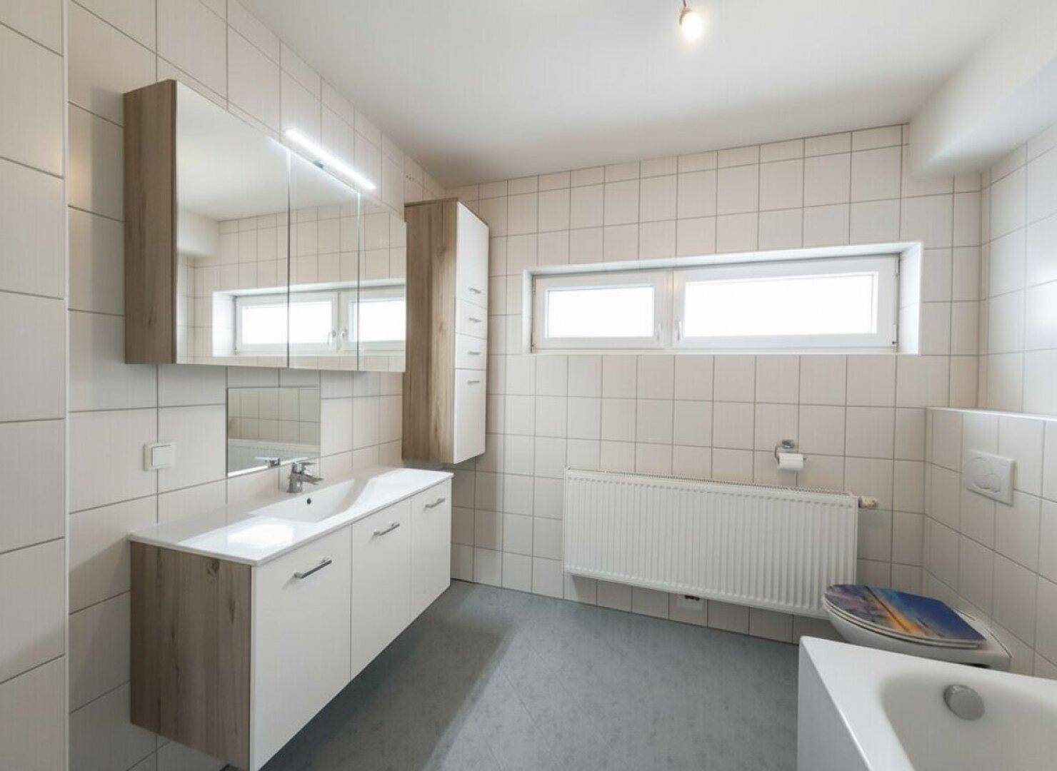 Helles Badezimmer mit Waschtisch, Spiegelschrank und Fenster für natürliche Belüftung.