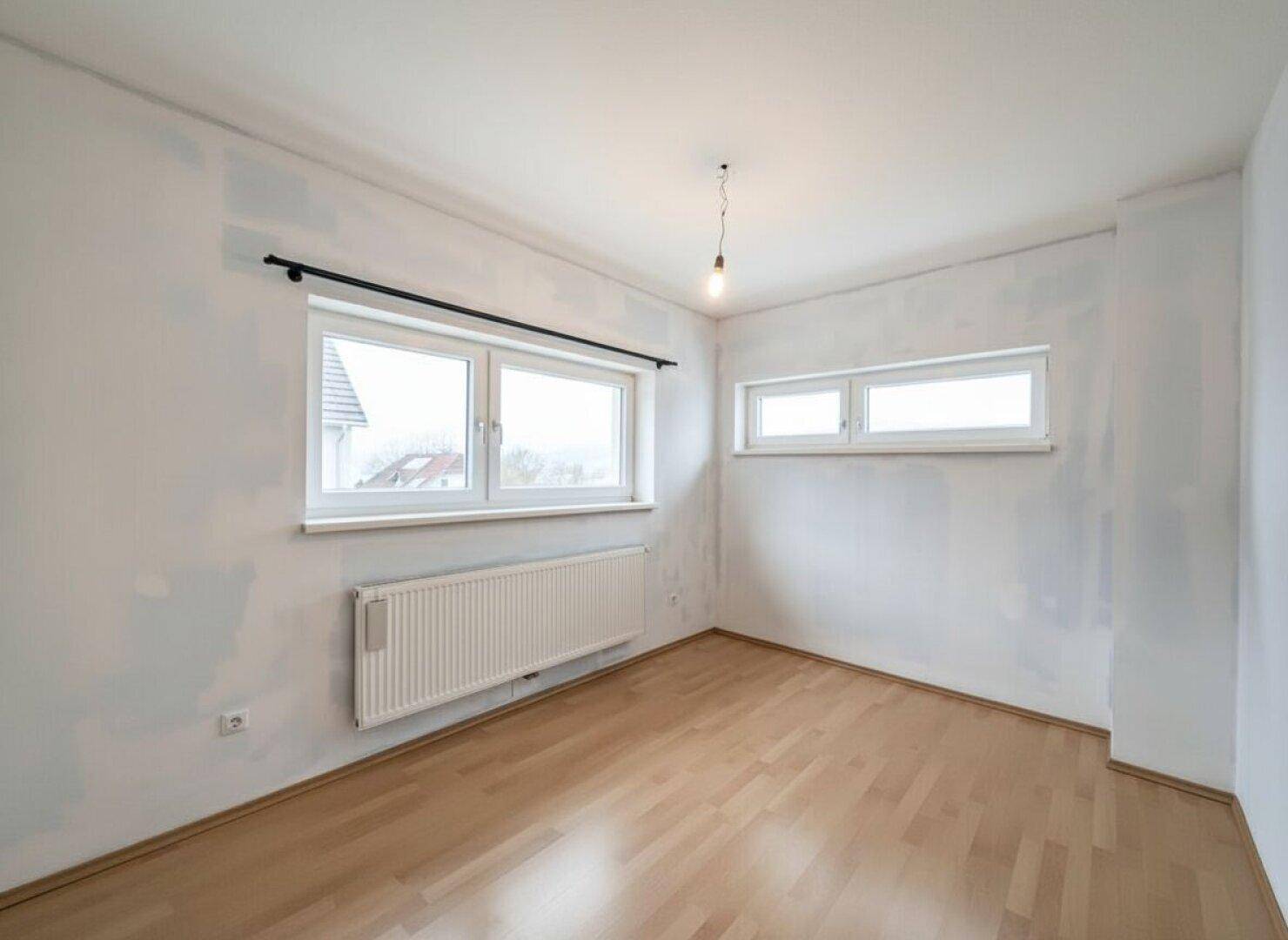 Helles Schlafzimmer mit zwei Fenstern und Parkettboden, bereit zur individuellen Gestaltung.