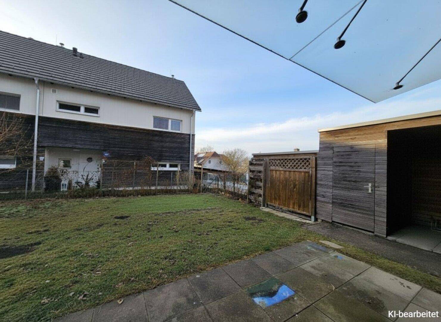 Gepflegter Gartenbereich mit Rasenfläche und einem Holzschuppen hinter dem Haus.