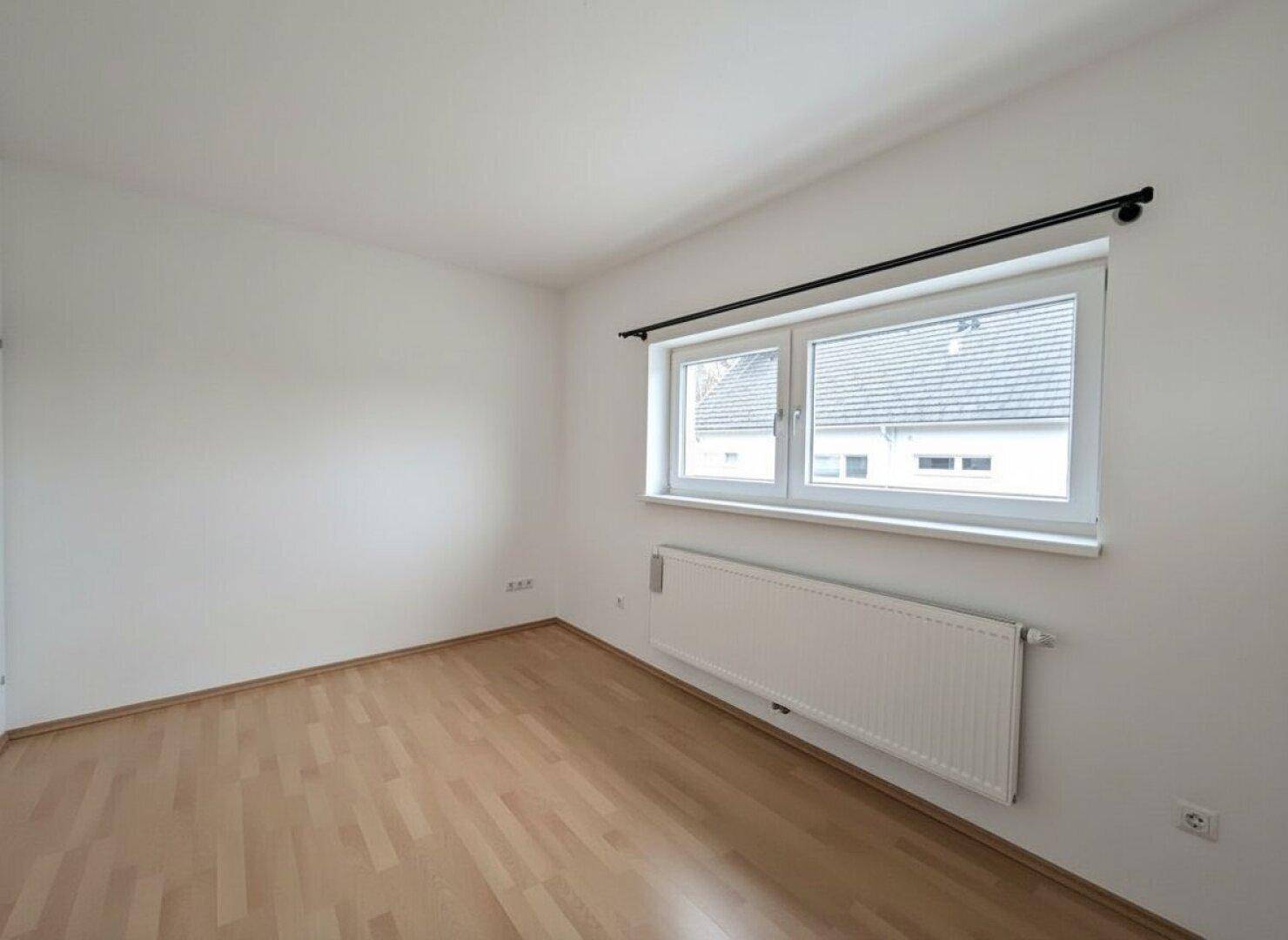 Helles Zimmer mit Parkettboden und großem Fenster, bietet viel Tageslicht.