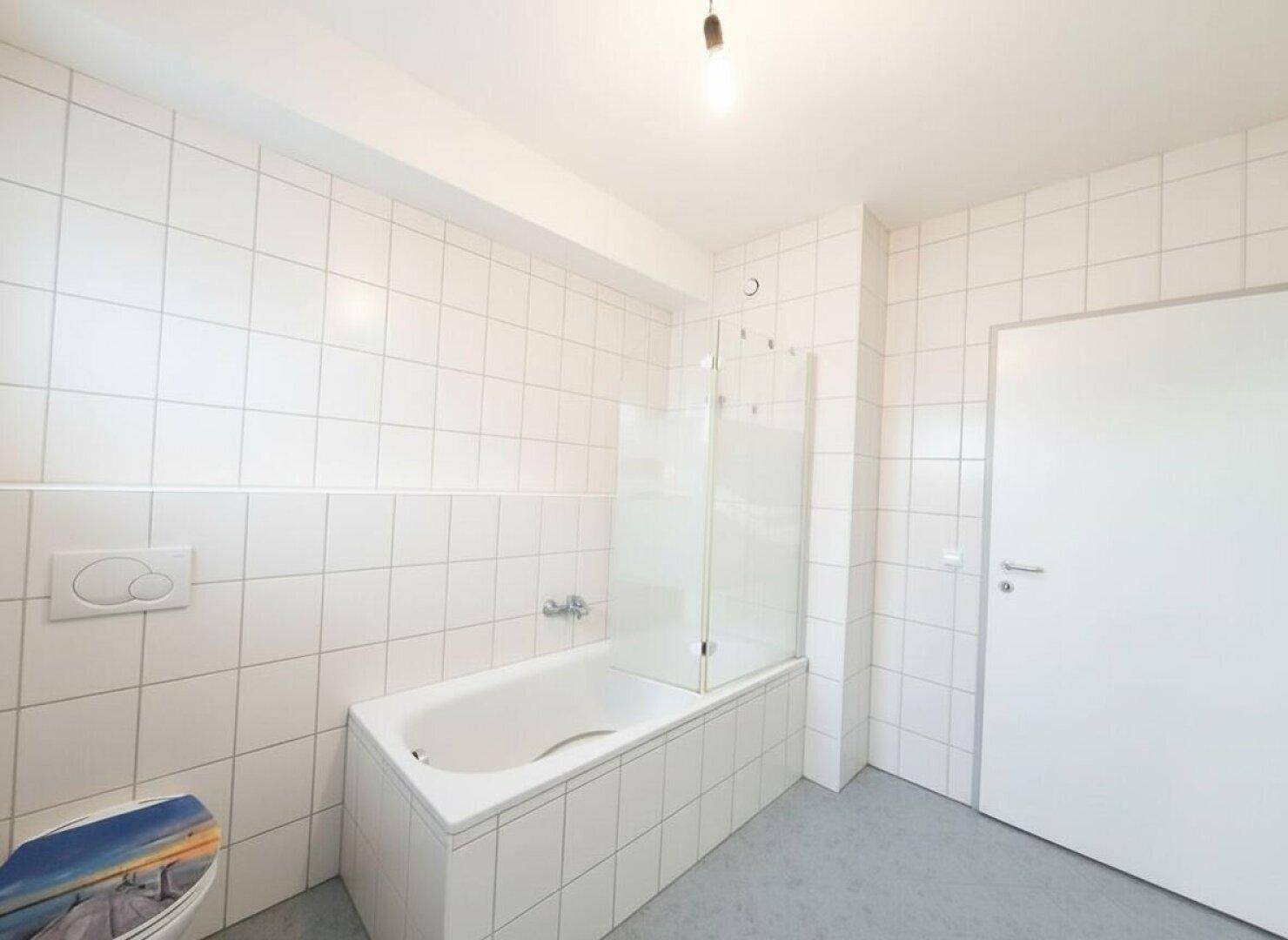 Modern gefliestes Badezimmer mit Badewanne und WC, in hellen Farbtönen gehalten.