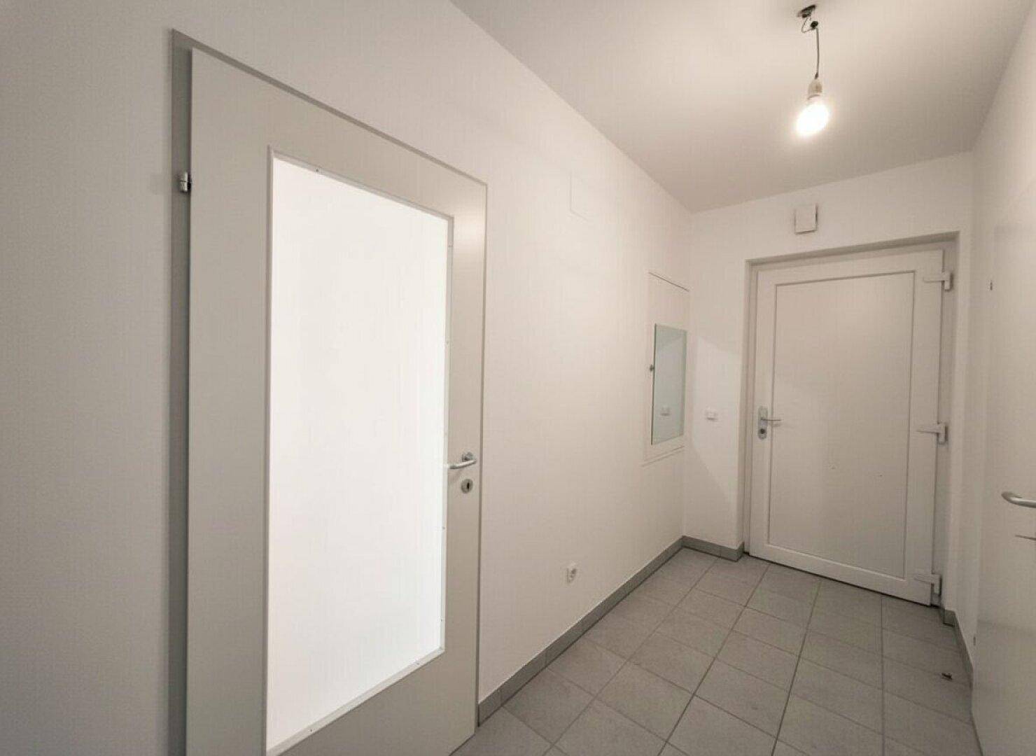 Freundlicher Flur mit Fliesenboden und einer Tür mit Glaseinsatz, die Licht hereinlässt.