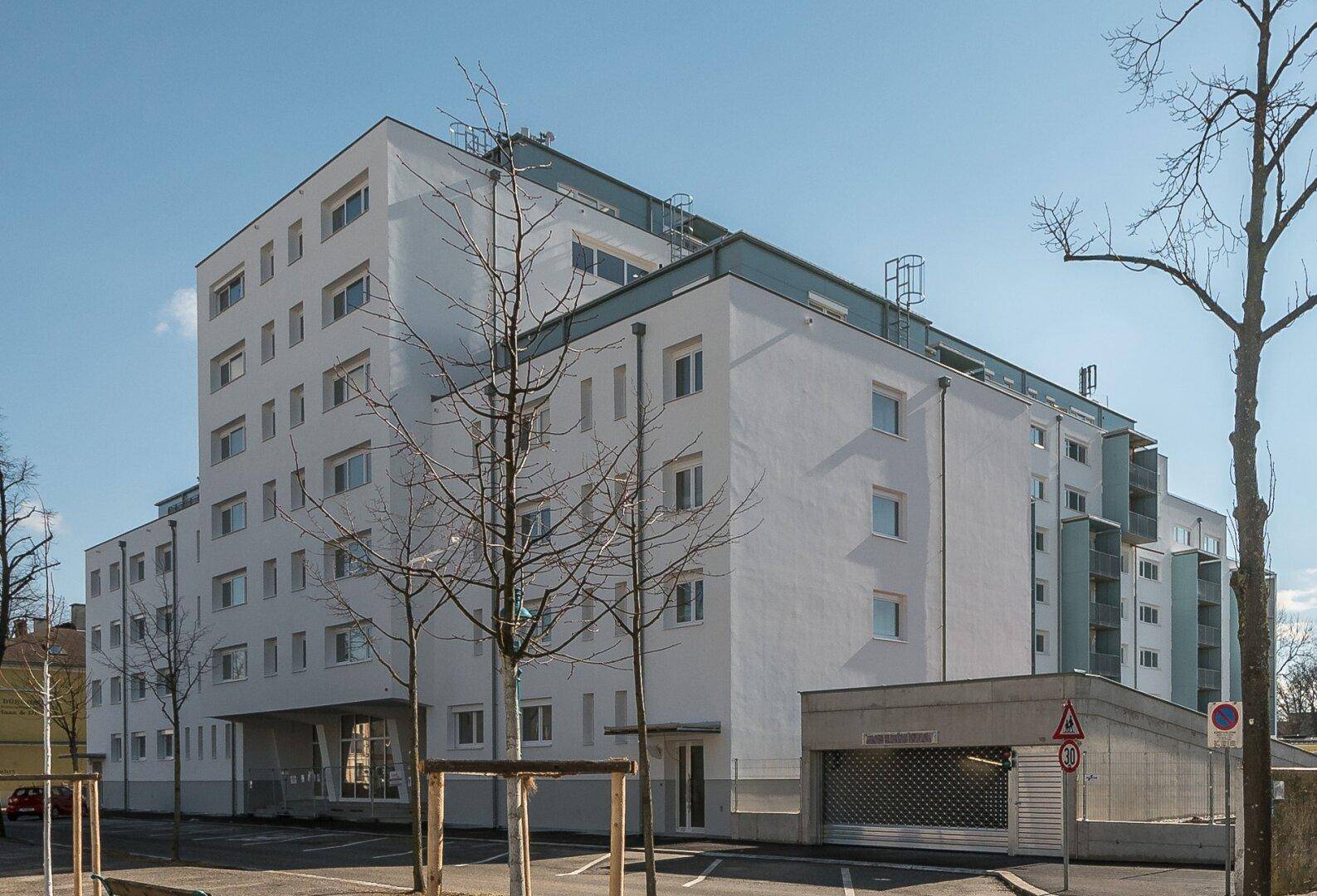 Modernes Mehrfamilienhaus mit weißer Fassade, vielen Fenstern und Tiefgaragenzufahrt.