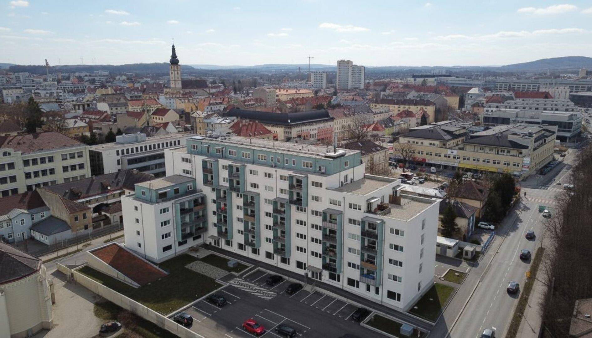 Luftaufnahme eines modernen Wohnkomplexes in einer städtischen Umgebung mit Kirchturm.