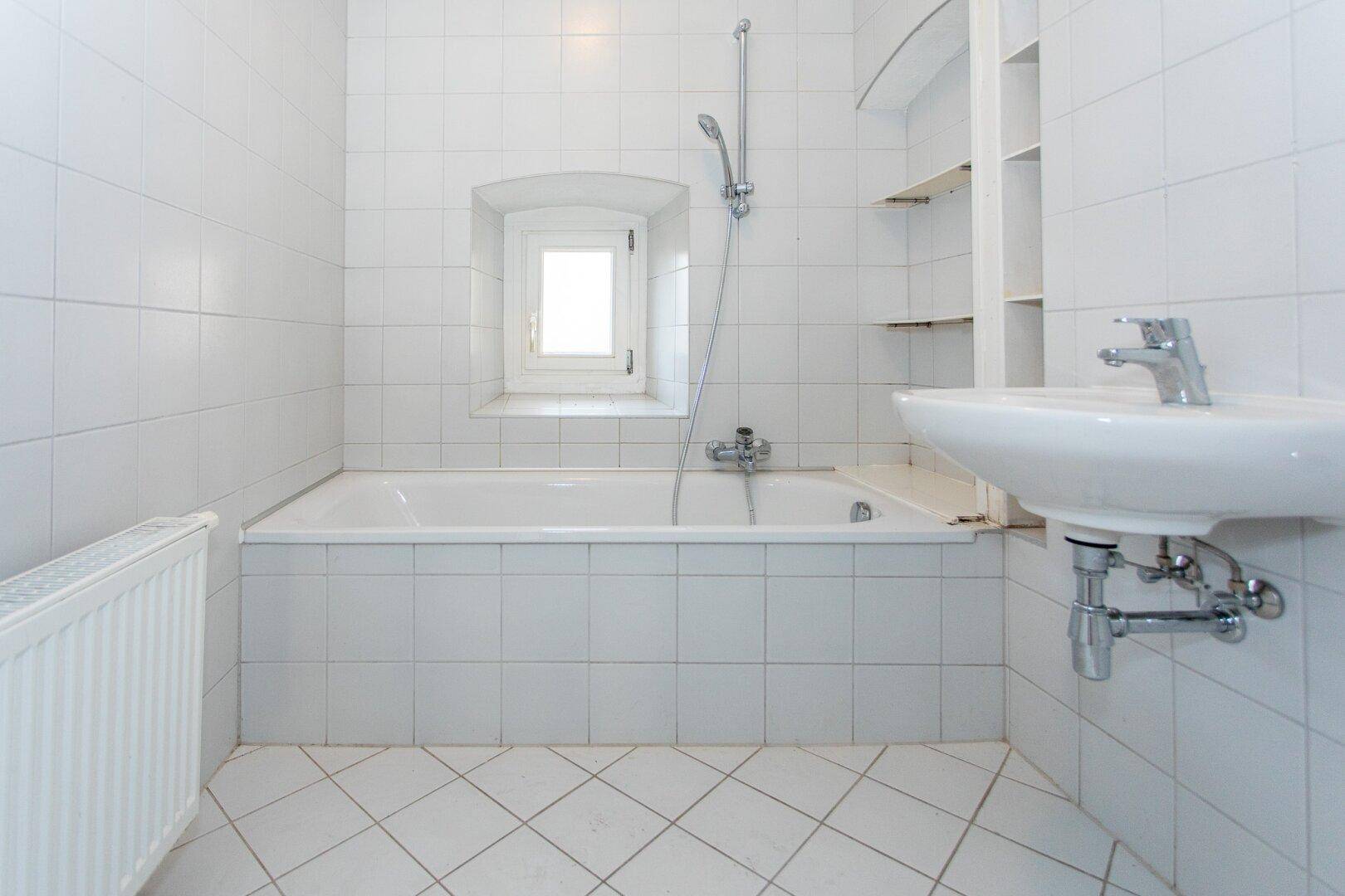 Gefliestes Badezimmer mit Badewanne, Waschbecken und Fenster, in gutem, funktionalem Zustand.