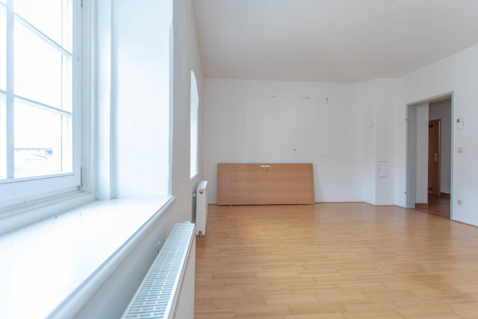 Heller Raum mit Parkettboden und großem Fenster, bietet viel Tageslicht und Gestaltungsmöglichkeiten.