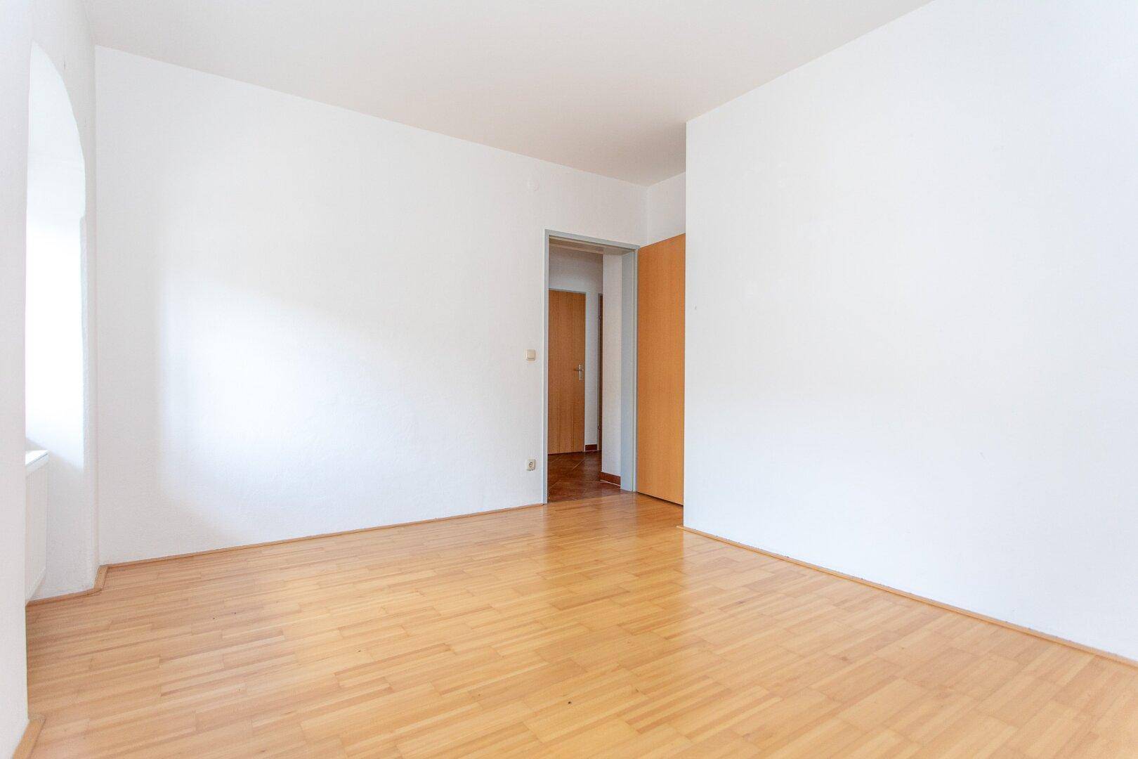 Leeres Zimmer mit Parkettboden und Zugang zu einem weiteren Raum, ideal für flexible Nutzung.