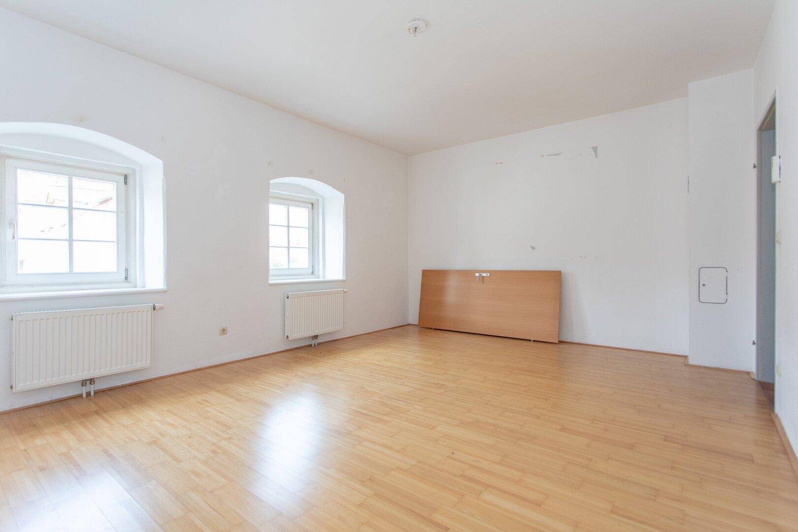 Geräumiges, helles Zimmer mit Parkettboden und zwei Fenstern, ideal für Wohn- oder Schlafbereich.