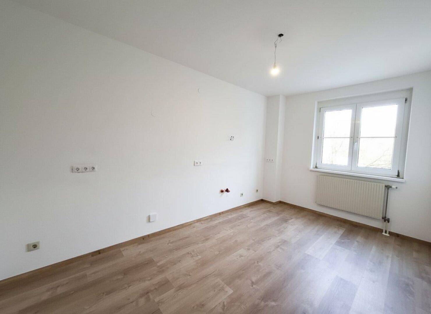 Leeres Zimmer mit Laminatboden und einem Fenster, bereit für individuelle Einrichtung.
