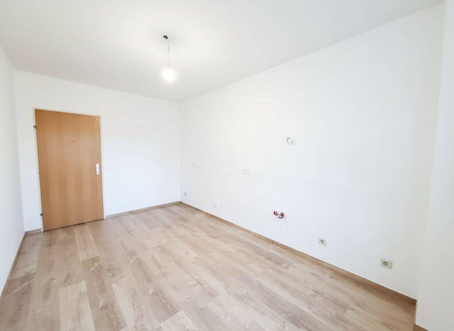 Leeres Zimmer mit Laminatboden und Holztür, bietet vielseitige Nutzungsmöglichkeiten.