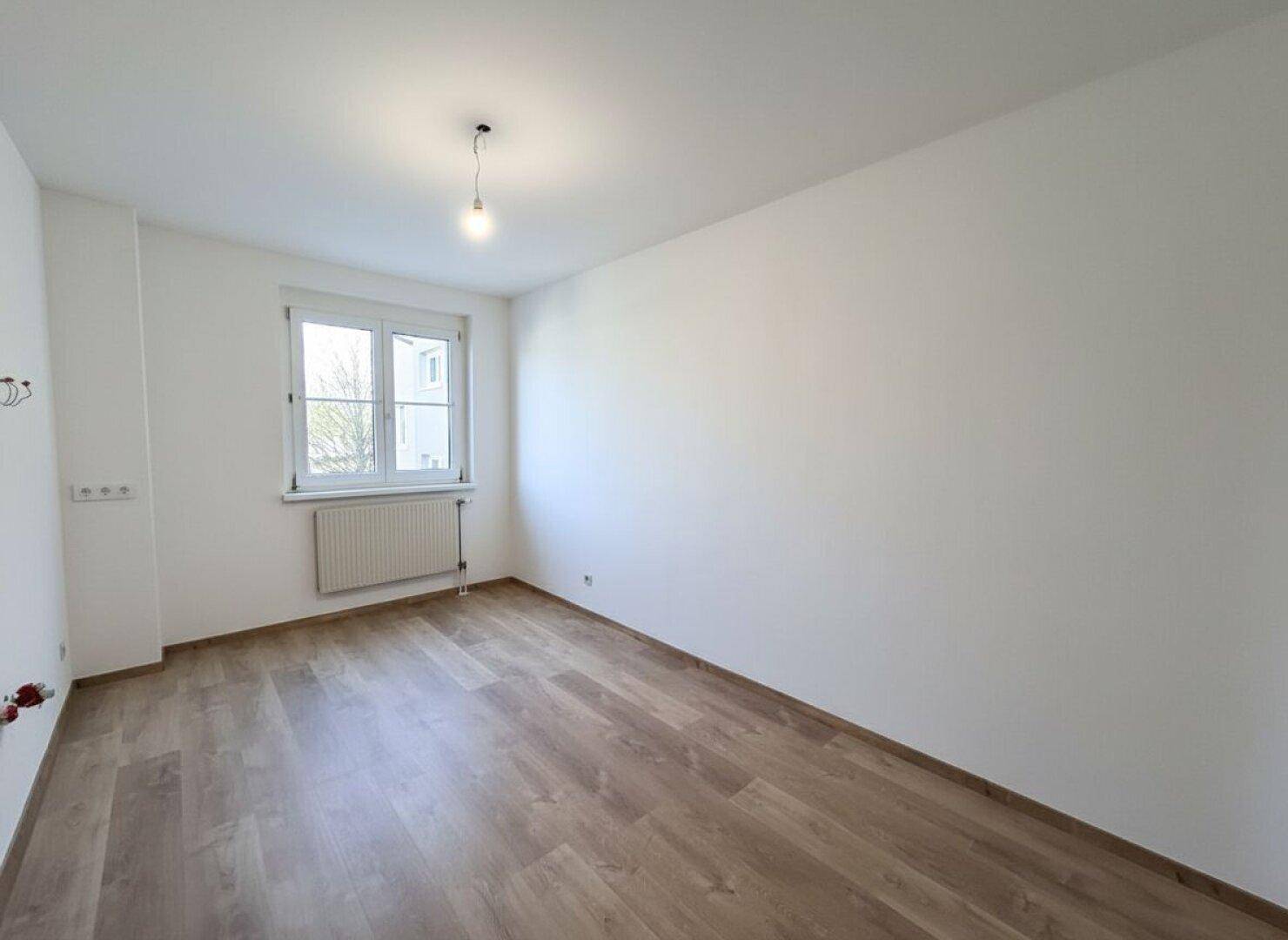 Helles Zimmer mit Laminatboden und weiß gestrichenen Wänden, ideal als Schlafzimmer.