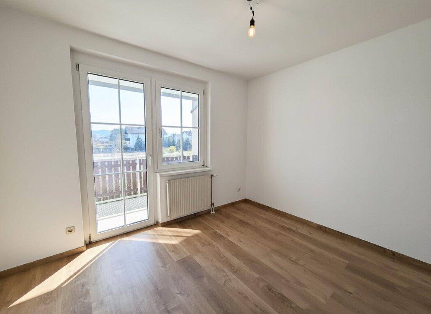 Helles Schlafzimmer mit Laminatboden und direktem Zugang zum Balkon.