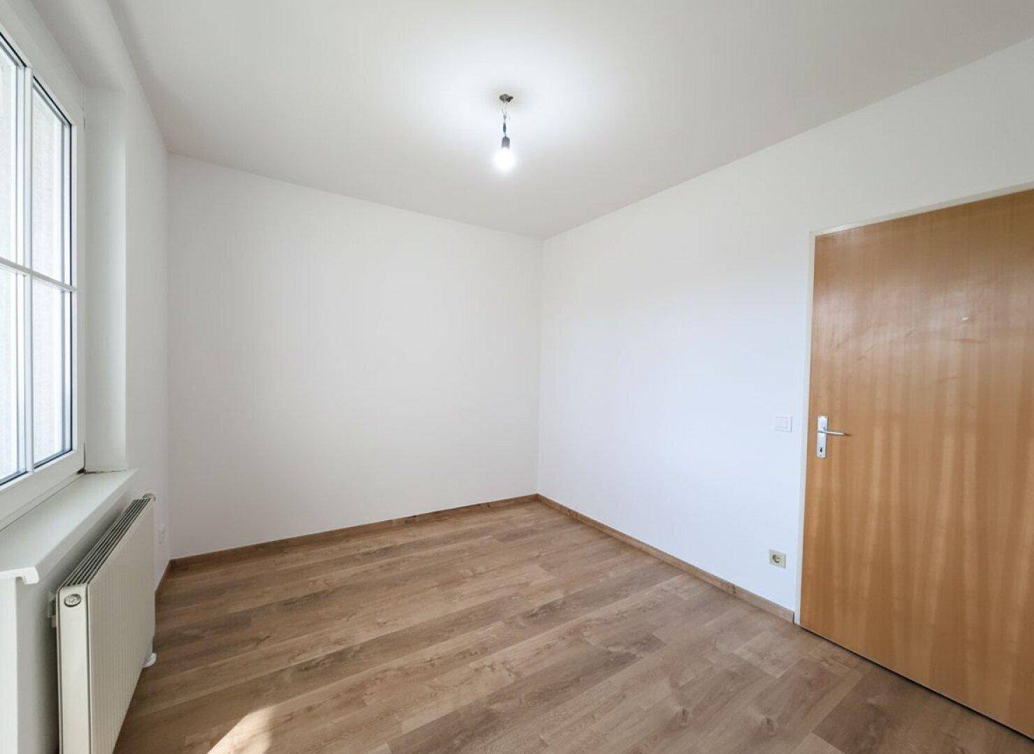 Helles Zimmer mit Laminatboden und Fenster, ideal als Kinder- oder Gästezimmer.