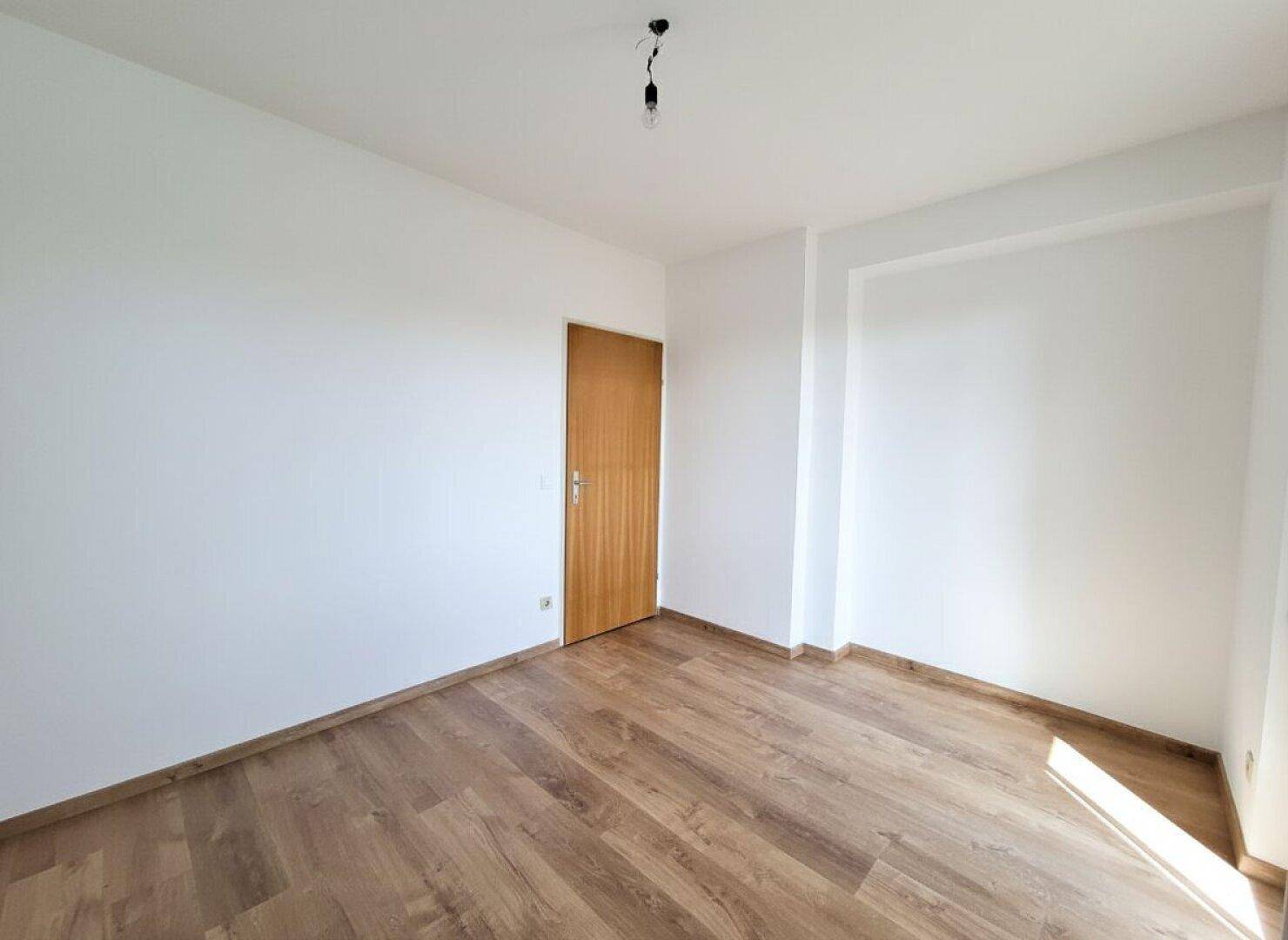 Leeres Schlafzimmer mit Laminatboden und Holztür, bereit zur Einrichtung.