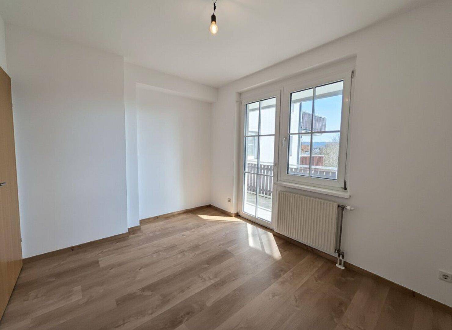 Geräumiges Schlafzimmer mit Laminatboden und Balkontür, lichtdurchflutet.