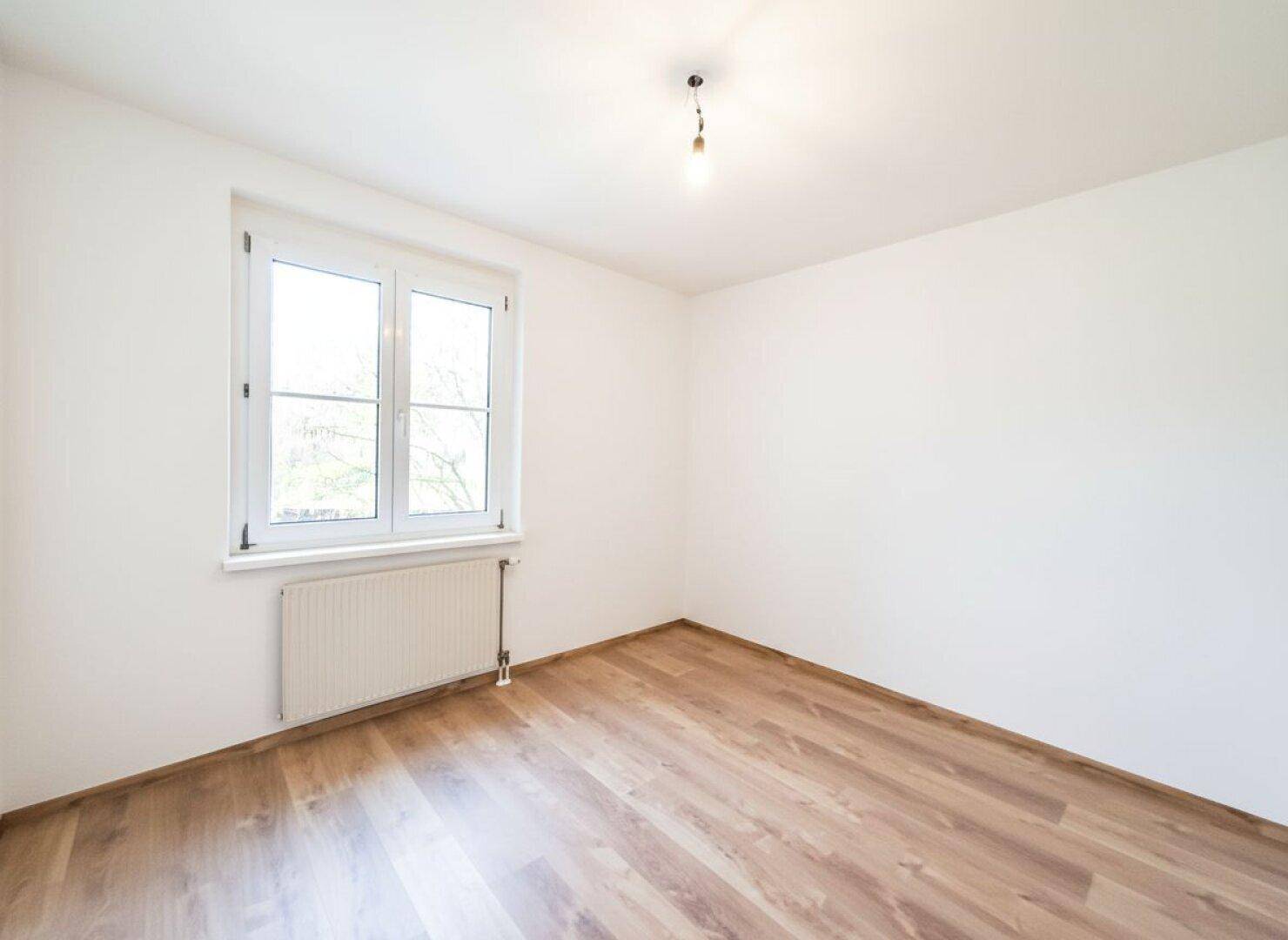 Leeres Zimmer mit Laminatboden und Fenster, bietet viel Tageslicht.