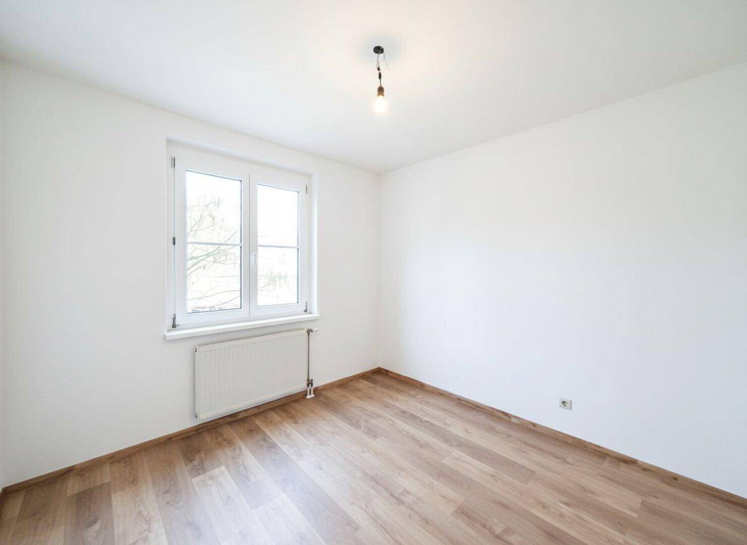 Geräumiges Zimmer mit Laminatboden und Fenster, ideal für ein Schlafzimmer.