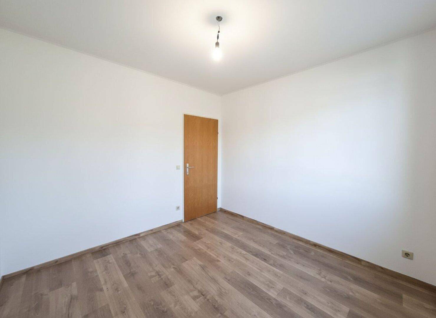 Leeres Zimmer mit Laminatboden und Holztür, bietet eine neutrale Basis.