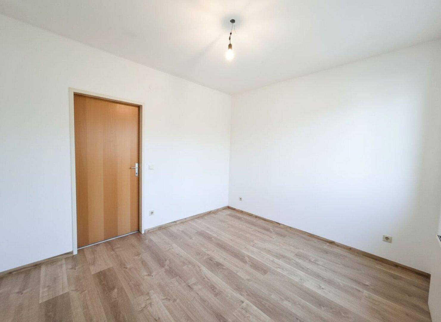 Helles Zimmer mit Laminatboden und Holztür, bereit zur individuellen Gestaltung.