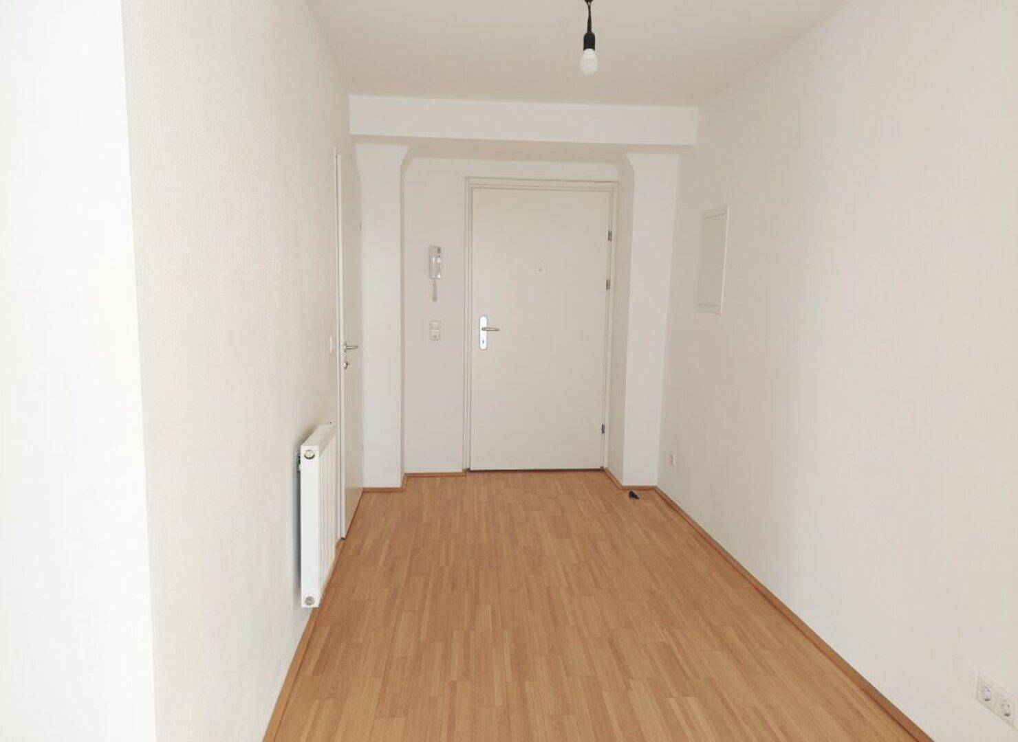 Heller Flur mit Parkettboden und Eingangstür, die in die Wohnung führt.