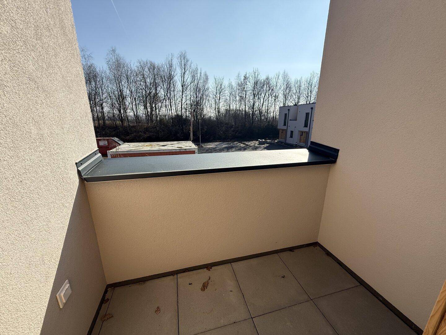 Kleiner Balkon mit Fliesenboden und Blick auf die umliegende grüne Landschaft und Gebäude.