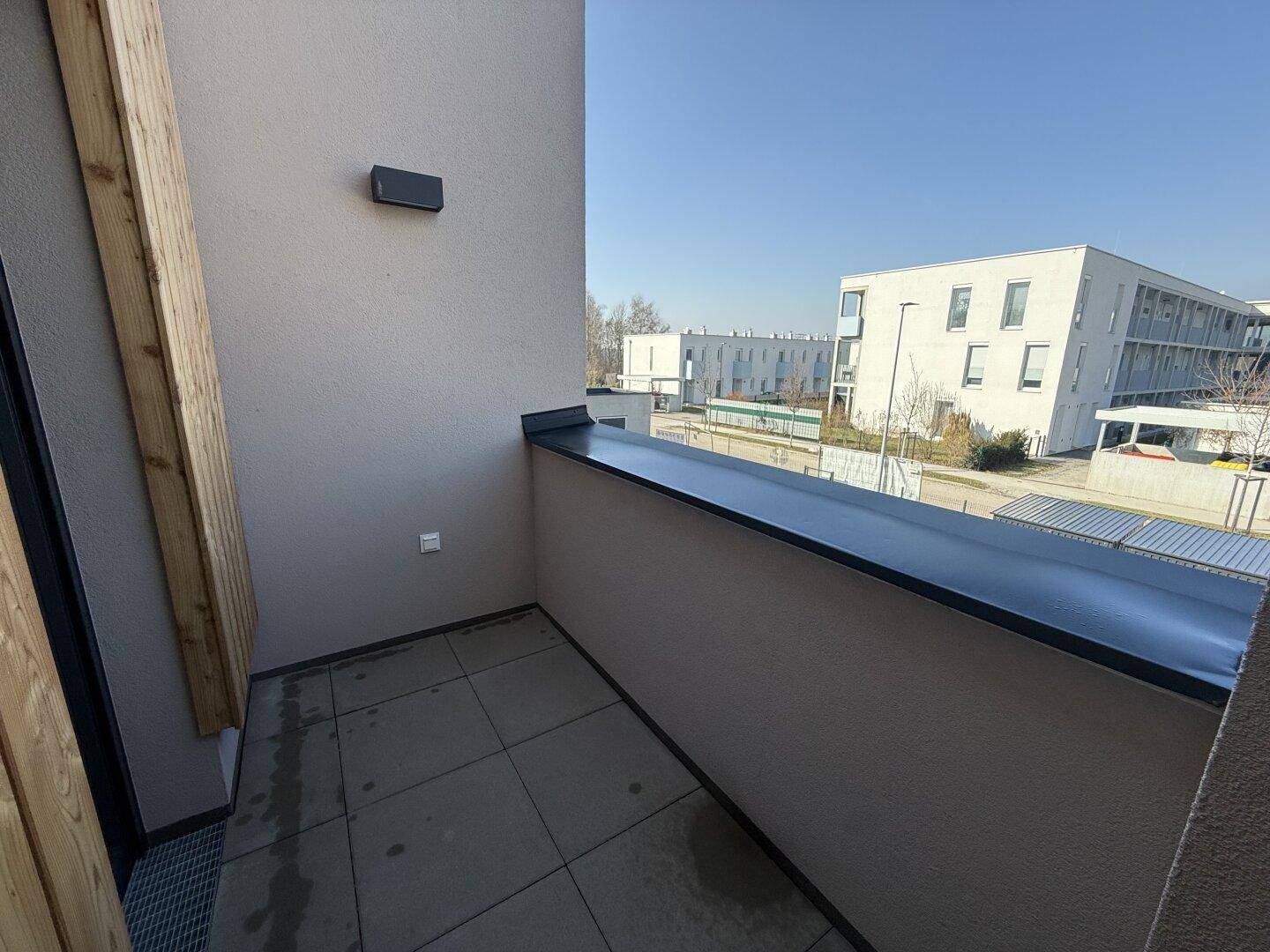 Kleiner Balkon mit Fliesenboden und Blick auf die modernen Wohngebäude der Nachbarschaft.