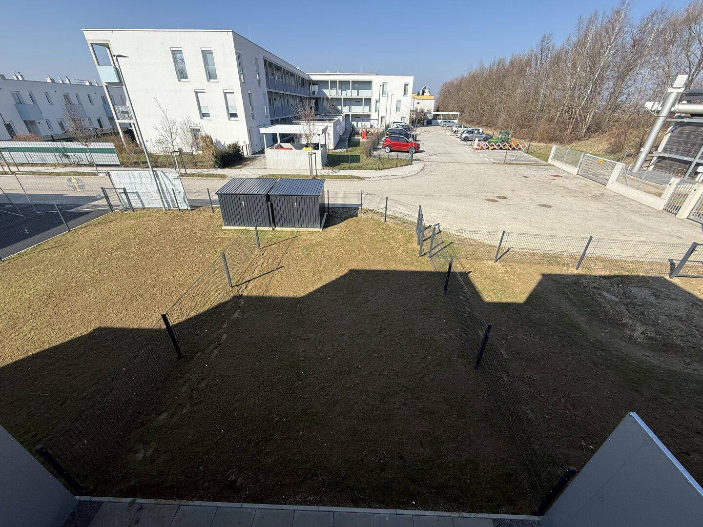 Blick von oben auf eine Grünfläche, Parkplätze und moderne Wohngebäude in der Umgebung.