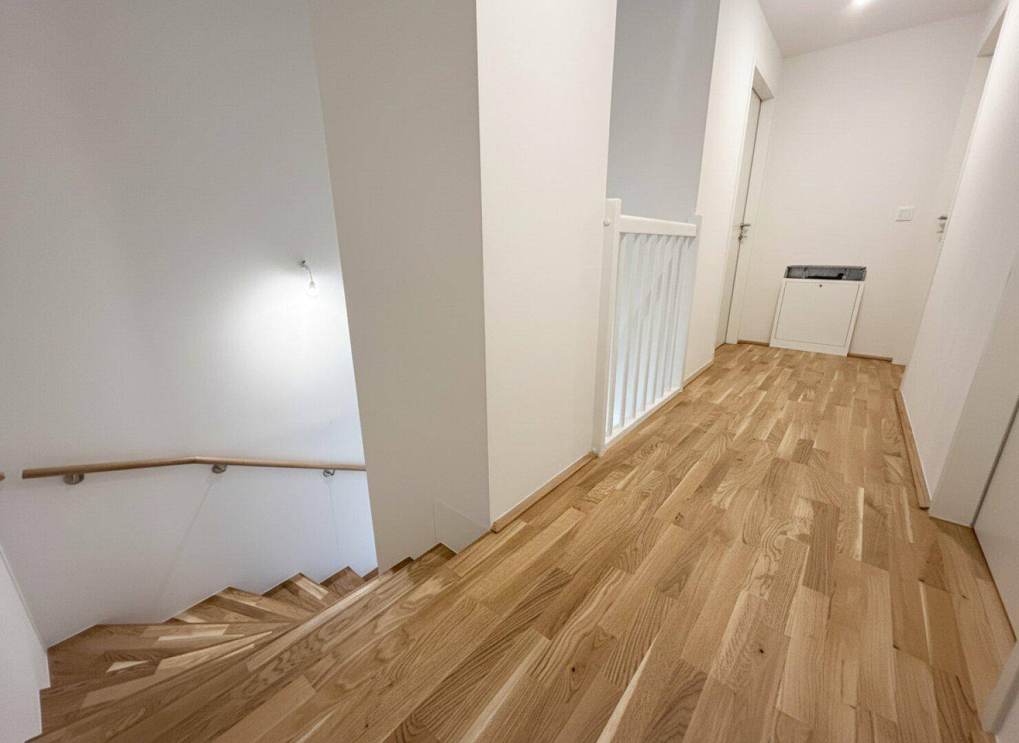 Heller Flur mit Holztreppe und Parkettboden, der die verschiedenen Ebenen des Hauses verbindet.