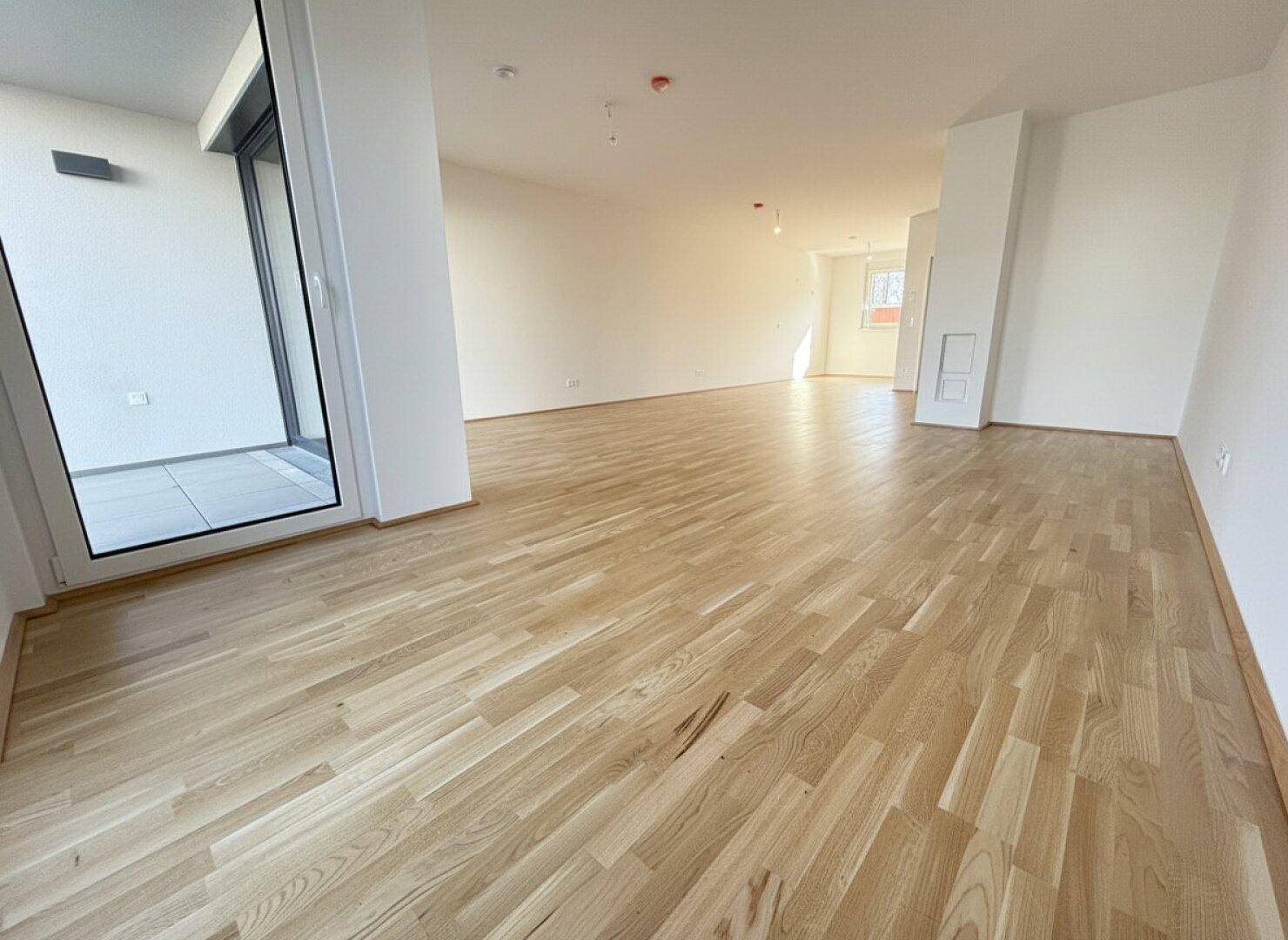 Großzügiger, offener Wohnbereich mit Parkettboden und viel Tageslicht durch die breite Fensterfront.