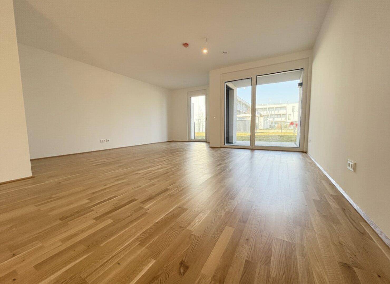 Geräumiges Wohnzimmer mit glänzendem Parkettboden und großen Fenstern, die viel Licht spenden.