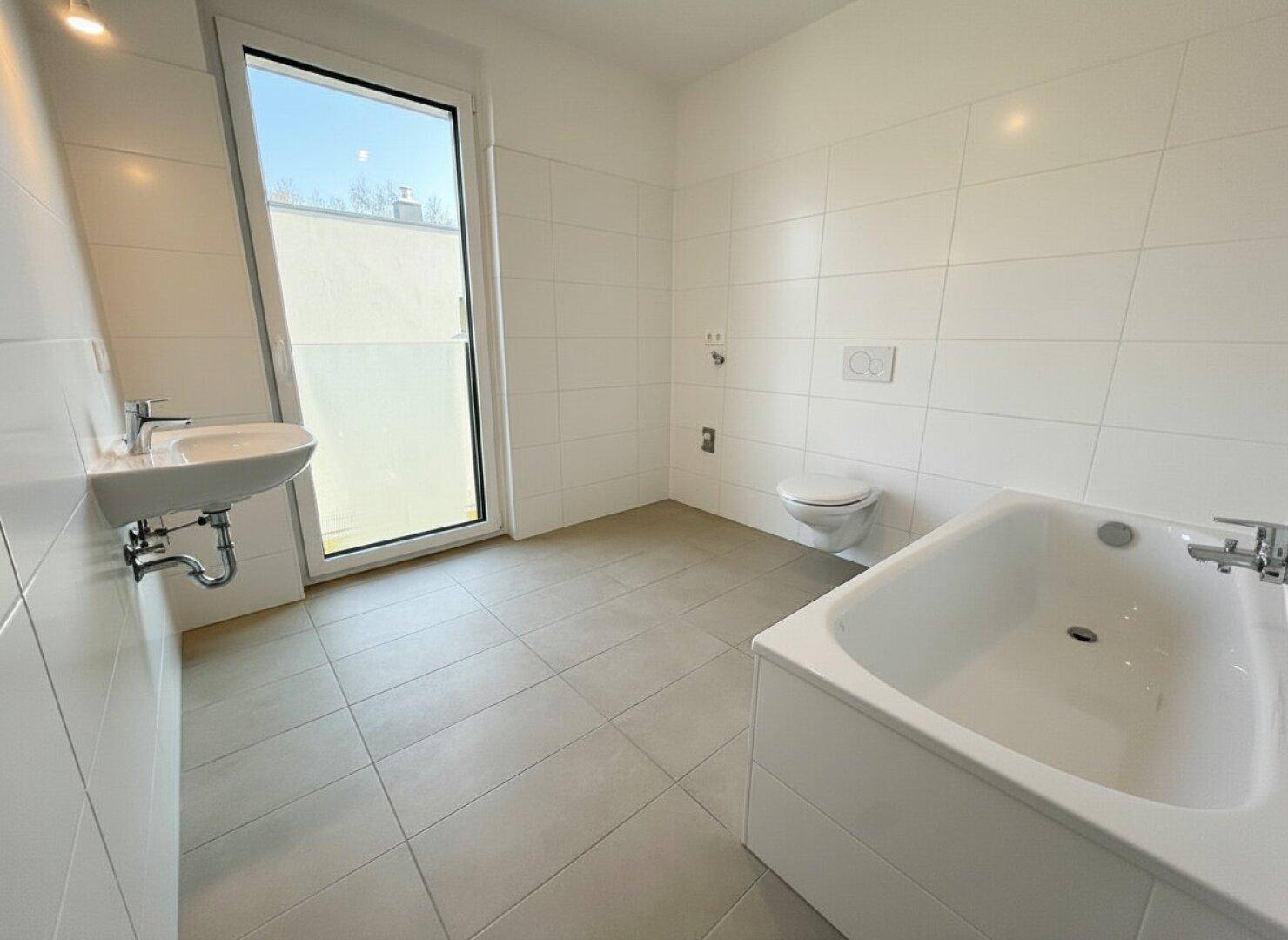 Helles Badezimmer mit Badewanne, WC, Waschbecken und einem großen Fenster für Tageslicht.